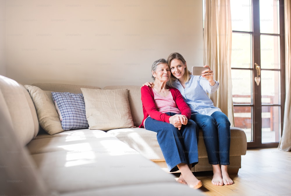 연로한 할머니와 성인 손녀가 집에서 스마트폰을 들고 셀카를 찍고 있다.