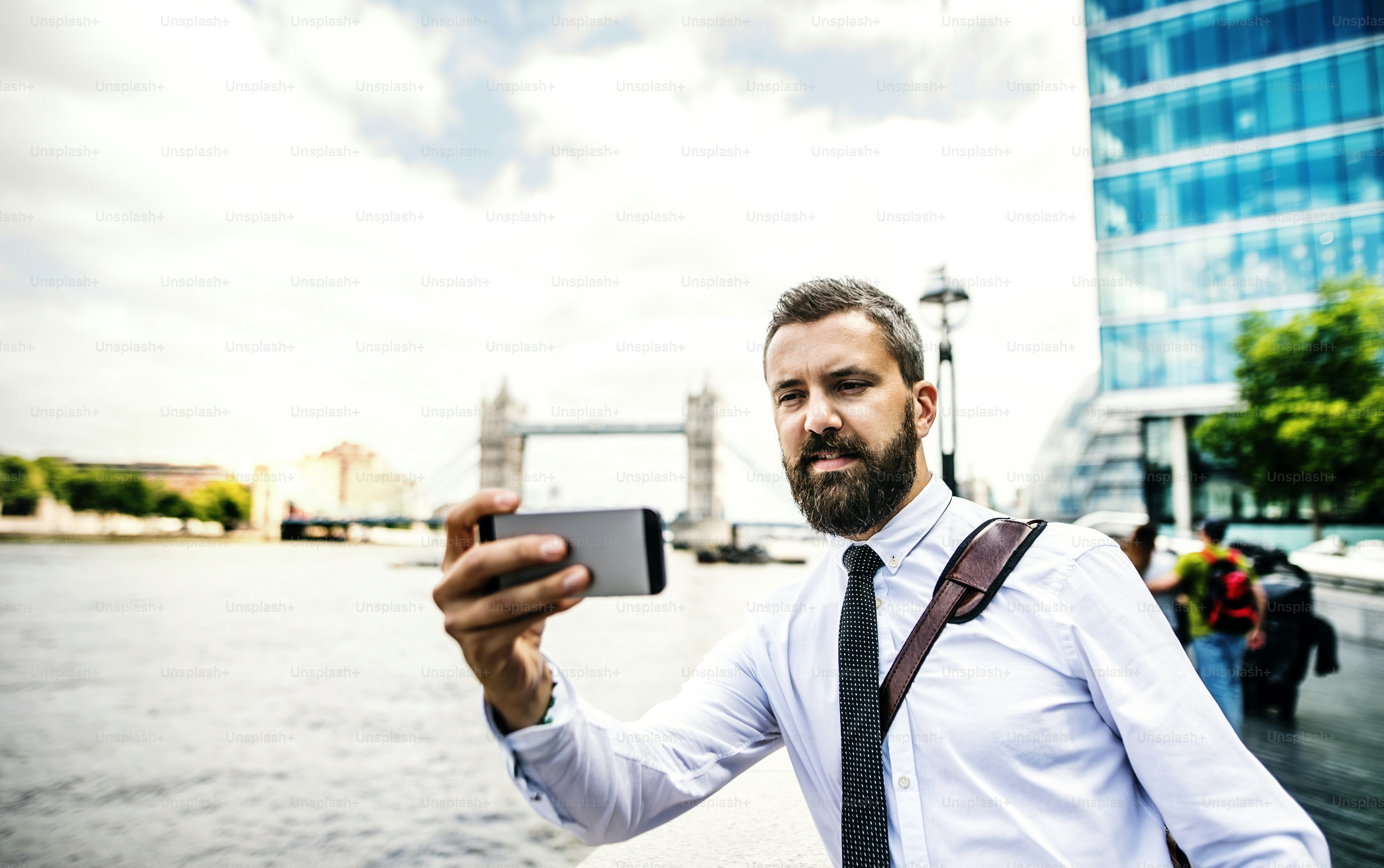 Hombre de negocios hipster con teléfono inteligente parado junto al río Támesis en Londres, tomándose selfie. Espacio de copia.
