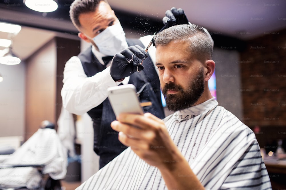 Handsome hipster man client visiting haidresser and hairstylist in barber shop, taking selfie with smartphone.