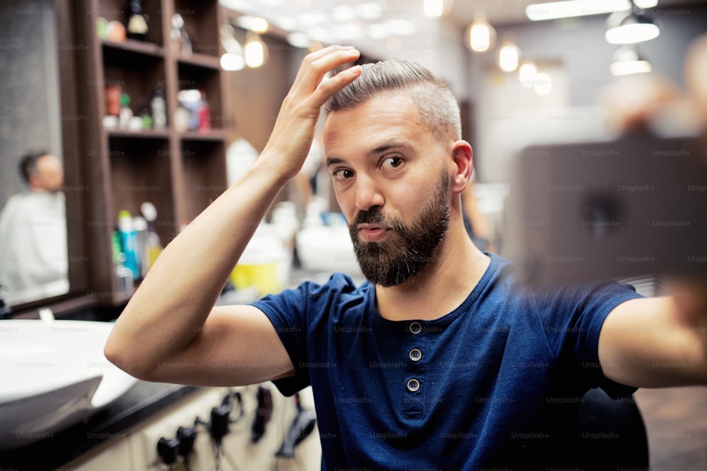 Un cliente hipster en una peluquería, haciendo caras divertidas al tomar seflie.