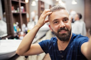 A hipster man client in barber shop, taking seflie. Copy space.