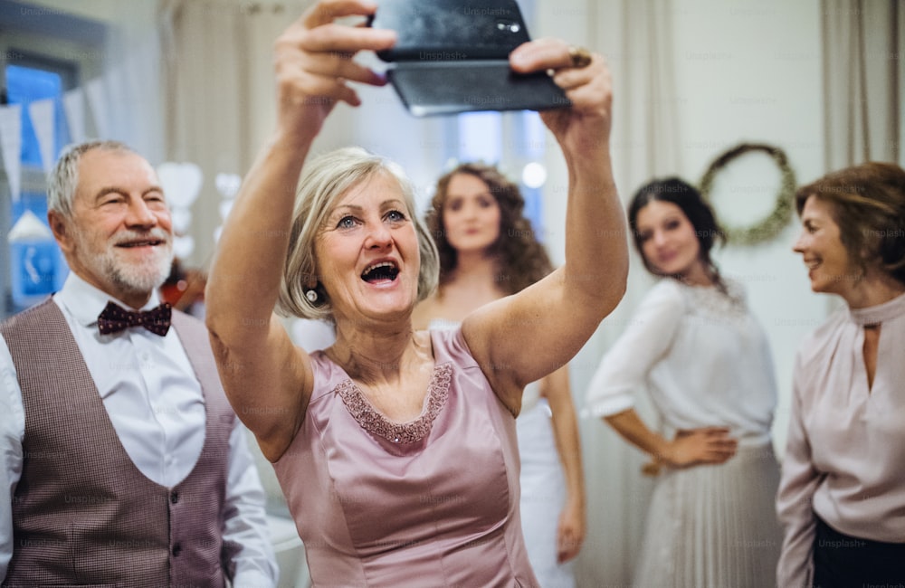 Una donna anziana felice con il marito alla festa di matrimonio o di compleanno, scattando selfie con lo smartphone.