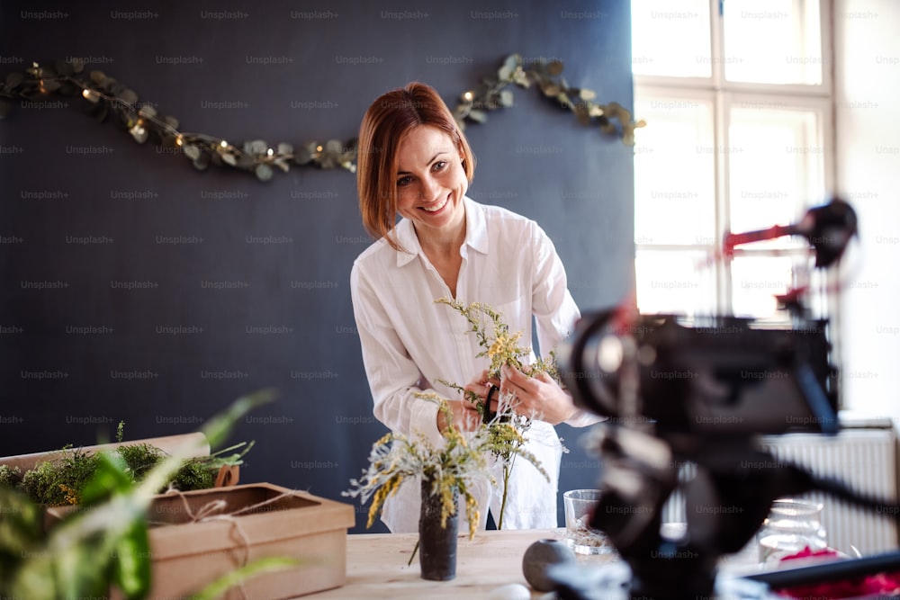 젊은 크리에이티브 여성 블로거 또는 블로거가 꽃집에서 꽃꽂이를 하고 있다. 플로리스트 사업의 창업.