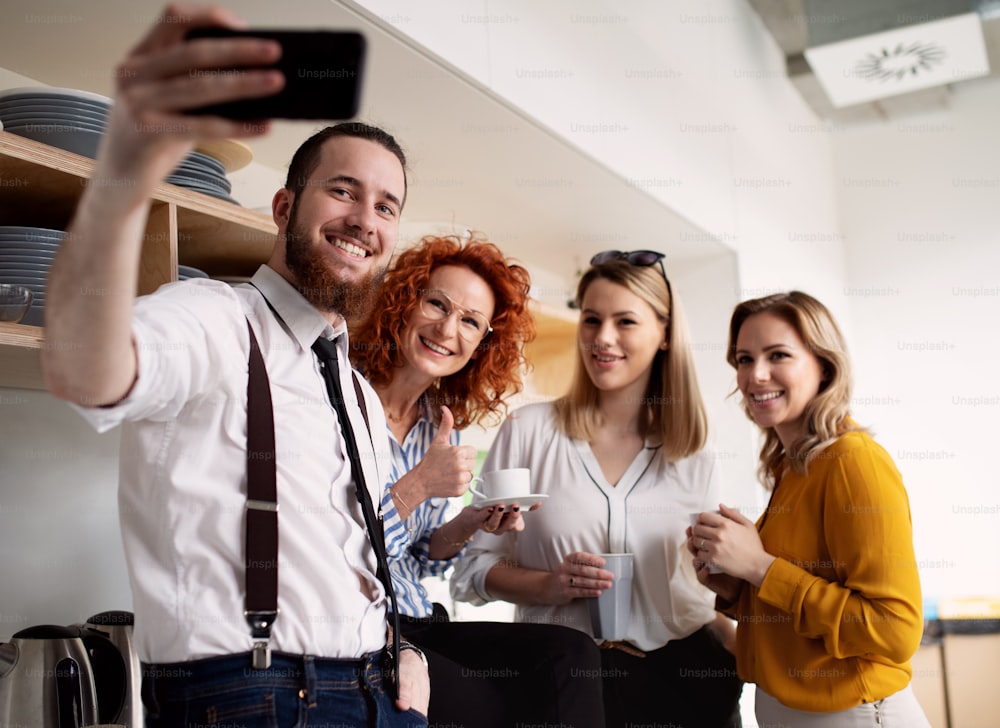 Un grupo de empresarios jóvenes y maduros con smartphone en el trabajo, tomándose selfie.