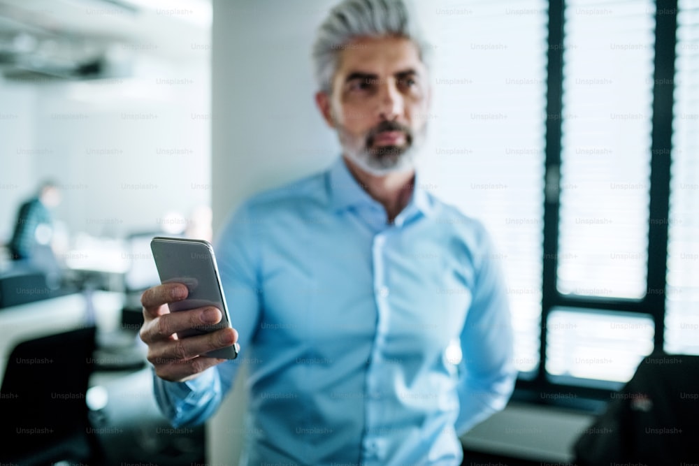 Portrait of young businessman with smartphone standing in an office, taking selfie.