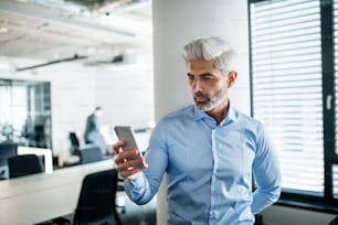 Ritratto di uomo d'affari maturo con smartphone in piedi in un ufficio, scattando selfie.