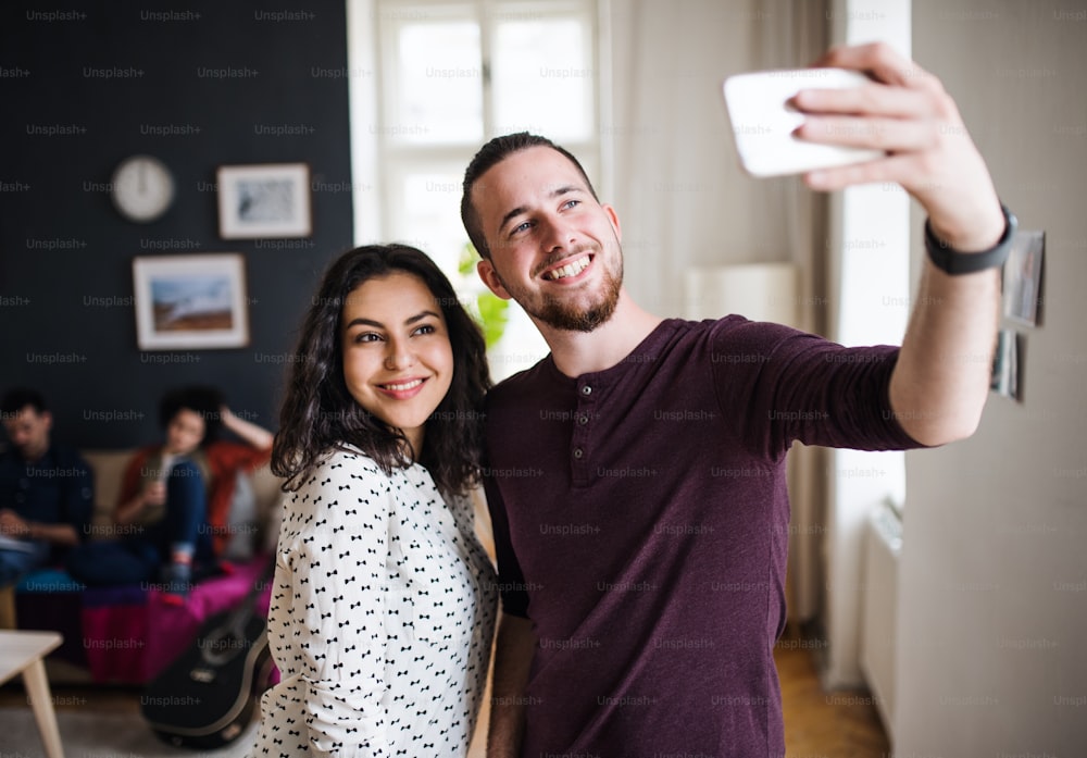 Eine Gruppe junger fröhlicher Freunde mit Smartphone drinnen, die Selfies machen. Wohngemeinschaftskonzept.