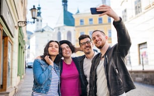 Un grupo de jóvenes amigos con un teléfono inteligente parado al aire libre en la ciudad, tomándose una selfie.