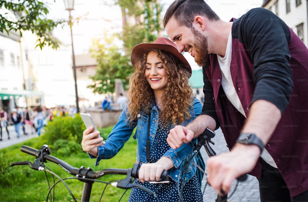 Jóvenes turistas que viajan en pareja con scooters eléctricos y teléfonos inteligentes en la ciudad, tomando selfies.