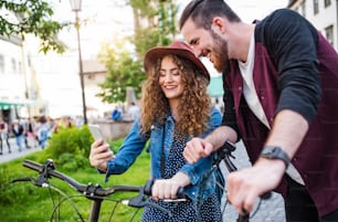 Jovem turista casal viajantes com scooters elétricas e smartphone na cidade, tirando selfie.