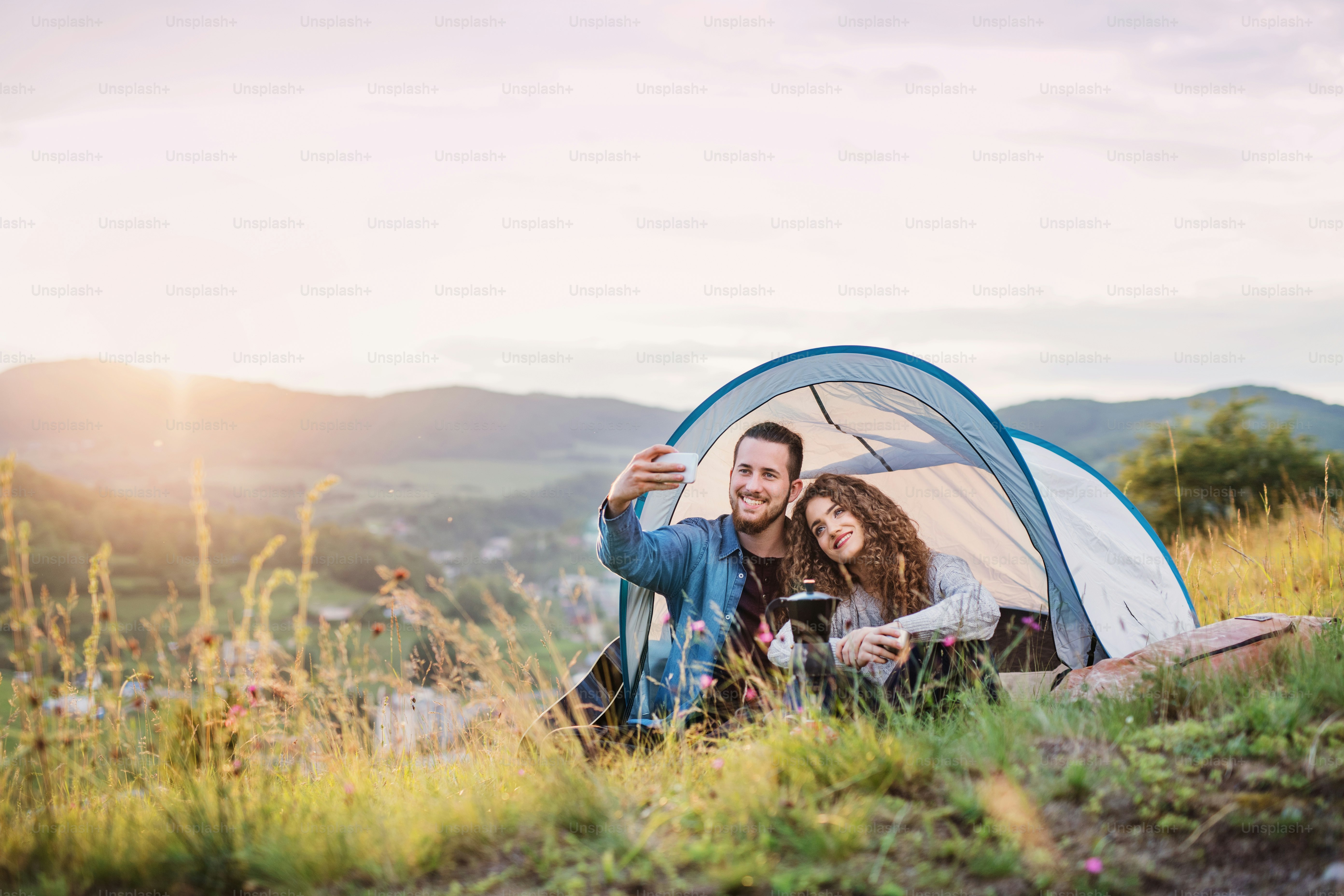 A young tourist couple travellers with tent shelter sitting in nature ...