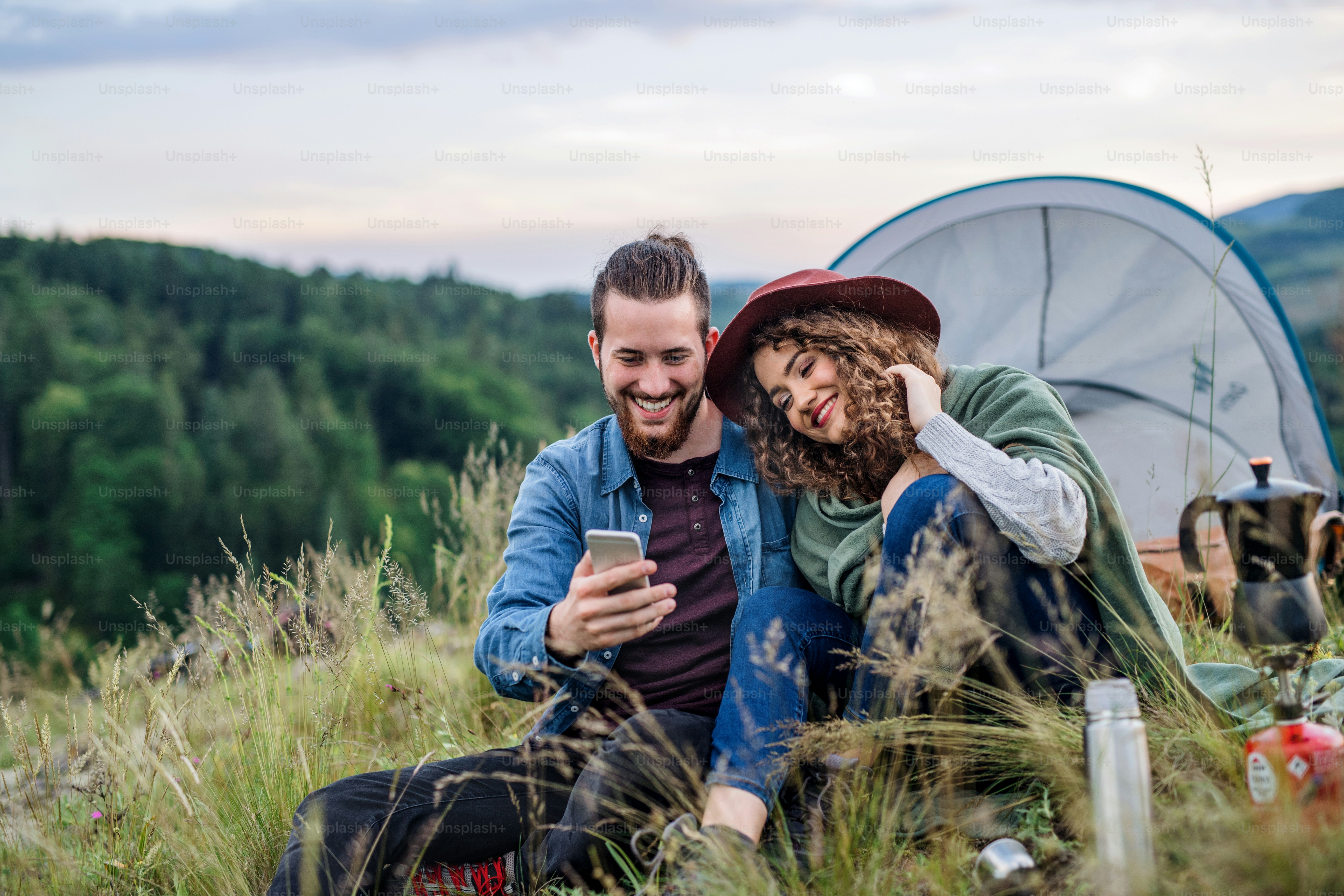 Traveler configuring remote internet hotspots beside a camping setup with laptop and gear