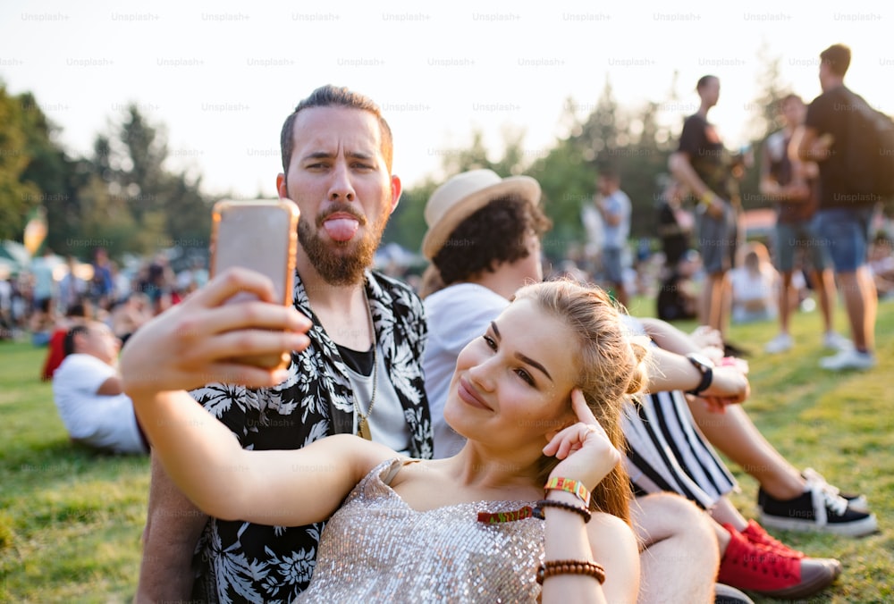 Front view portrait of young couple at summer festival, taking selfie with smartphone.