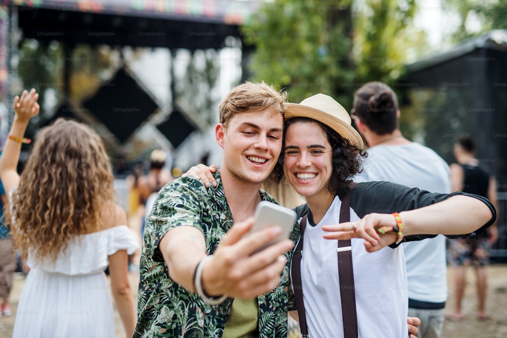 Front view portrait of young couple at summer festival, taking selfie with smartphone.