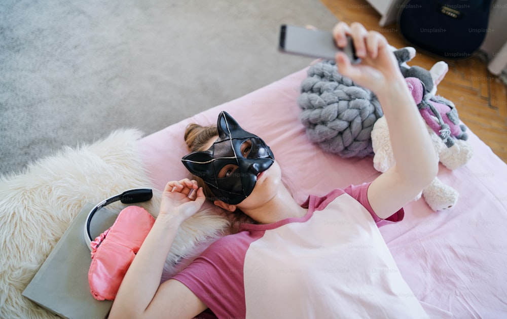 Vista superior de una niña con máscara de gato en la cama, tomando una selfie. Concepto de citas en línea.