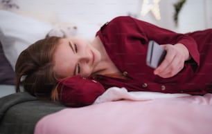 A happy young girl using smartphone on bed, online dating concept.