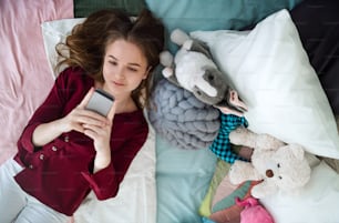 Top view of happy young girl smiling and taking selfie with smartphone on bed, online dating concept.