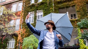 Porträt eines jungen Mannes mit Regenschirm, der ein Video im Freien auf der Straße macht, Social-Media-Konzept.
