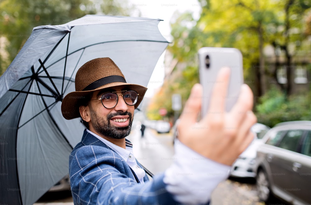 Portrait of young man with umbrella making video for social media outdoors on street.
