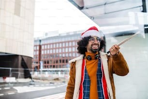 Jovem com chapéu de Papai Noel fazendo vídeo para as mídias sociais ao ar livre no ponto de ônibus. Espaço de cópia.