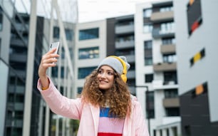 路上で屋外でソーシャルメディア用のビデオを作るスマートフォンを持つ若い女性のポートレート。