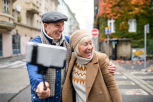Retrato de una feliz pareja de ancianos caminando al aire libre en la calle de la ciudad, tomándose una selfie.