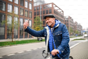 Happy senior man commuter with bicycle outdoors on street in city, taking selfie.