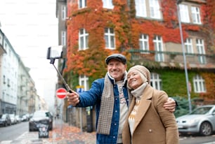 Portrait d’un couple de personnes âgées heureux marchant dehors dans la rue de la ville, prenant un selfie.