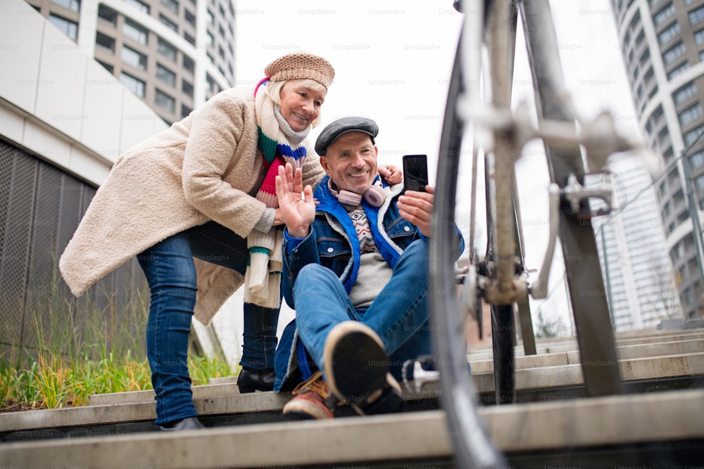 Portrait of happy senior couple outdoors on sidewalk in city, taking selfie.