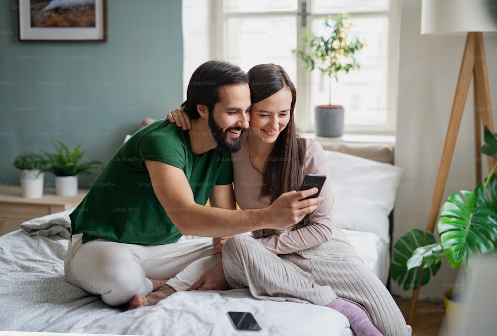 Happy young couple in love taking selfie on bed indoors at home.