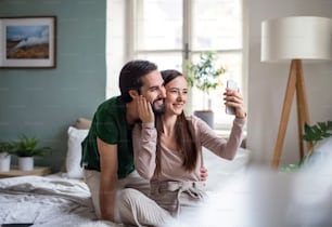 Jovem casal feliz apaixonado tirando selfie na cama dentro de casa.