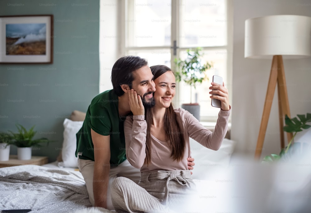 Feliz pareja joven enamorada tomándose selfie en la cama en el interior de casa.