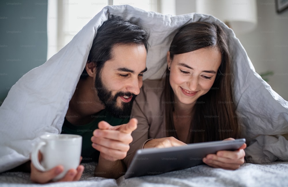 Feliz pareja joven enamorada usando tableta en la cama en el interior de casa.