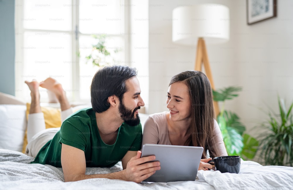 Happy young couple in love using tablet on bed indoors at home.