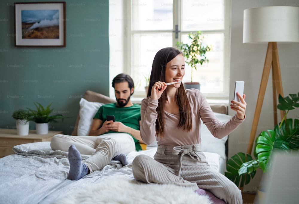 Glückliches junges Paar, das Smartphones auf dem Bett drinnen zu Hause benutzt.