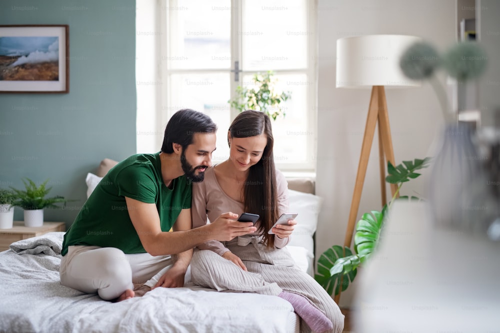Glückliches junges Paar, das Smartphones auf dem Bett drinnen zu Hause benutzt.