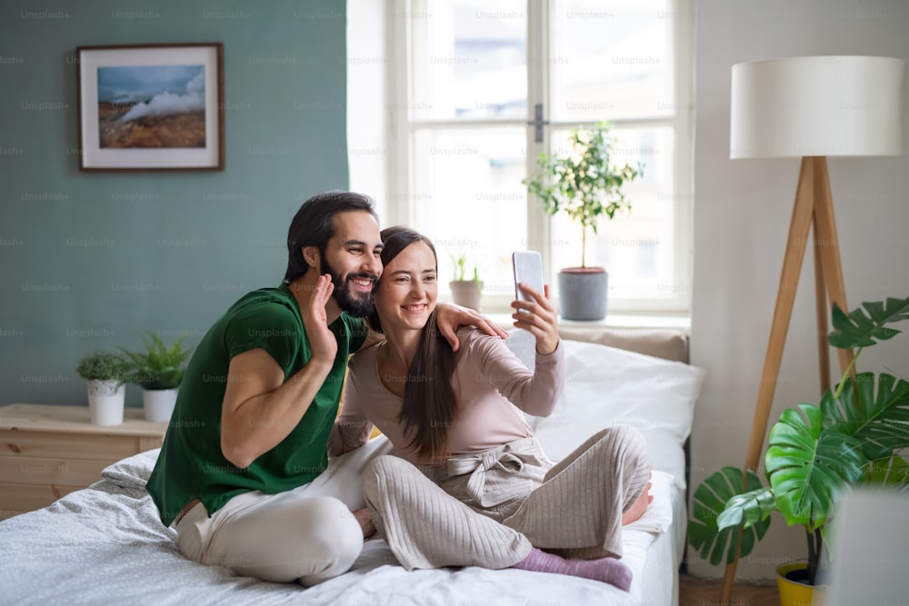 Jovem casal feliz tirando selfie na cama dentro de casa.