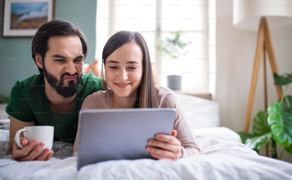Young couple with tablet on bed indoors at home, making funny faces.