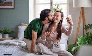 Happy young couple taking selfie in the morning on bed indoors at home.