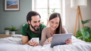 Happy young couple in love using tablet on bed indoors at home.