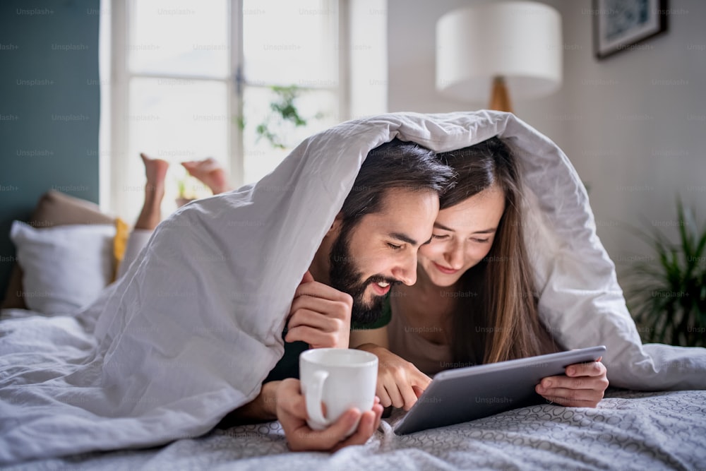 Feliz pareja joven enamorada usando tableta en la cama en el interior de casa.