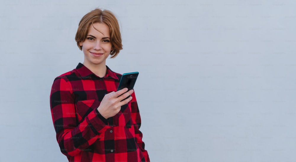 Una mujer joven con un teléfono inteligente sobre fondo blanco, mirando a la cámara.