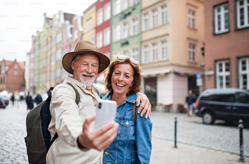 A portrait of happy senior couple tourists doing selfie outdoors in historic town