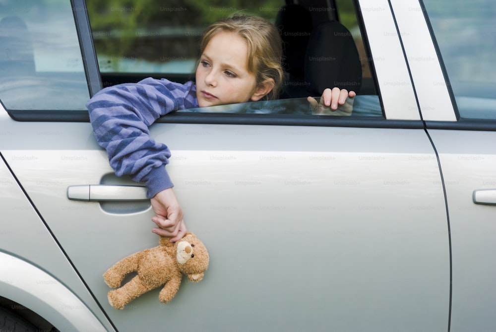 a young girl leaning out of a car window holding a teddy bear