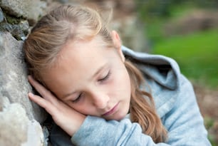 a young girl leaning against a stone wall