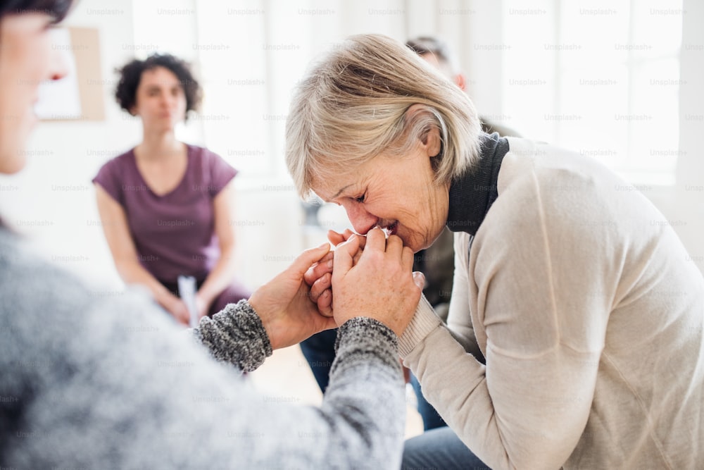 Una donna anziana depressa piange durante la terapia di gruppo, altre persone la confortano.