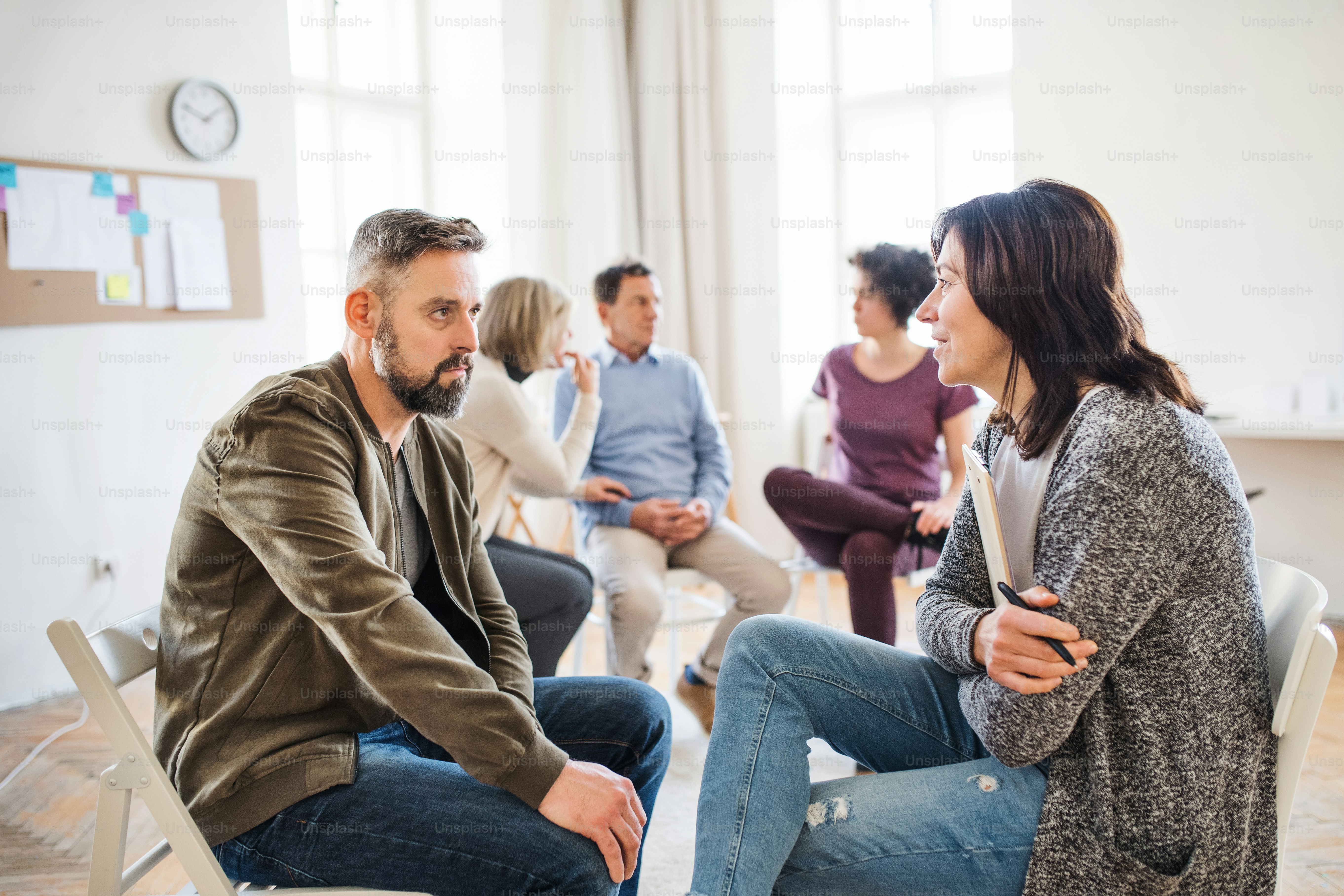 Um conselheiro sênior com prancheta conversando com um homem durante a terapia de grupo