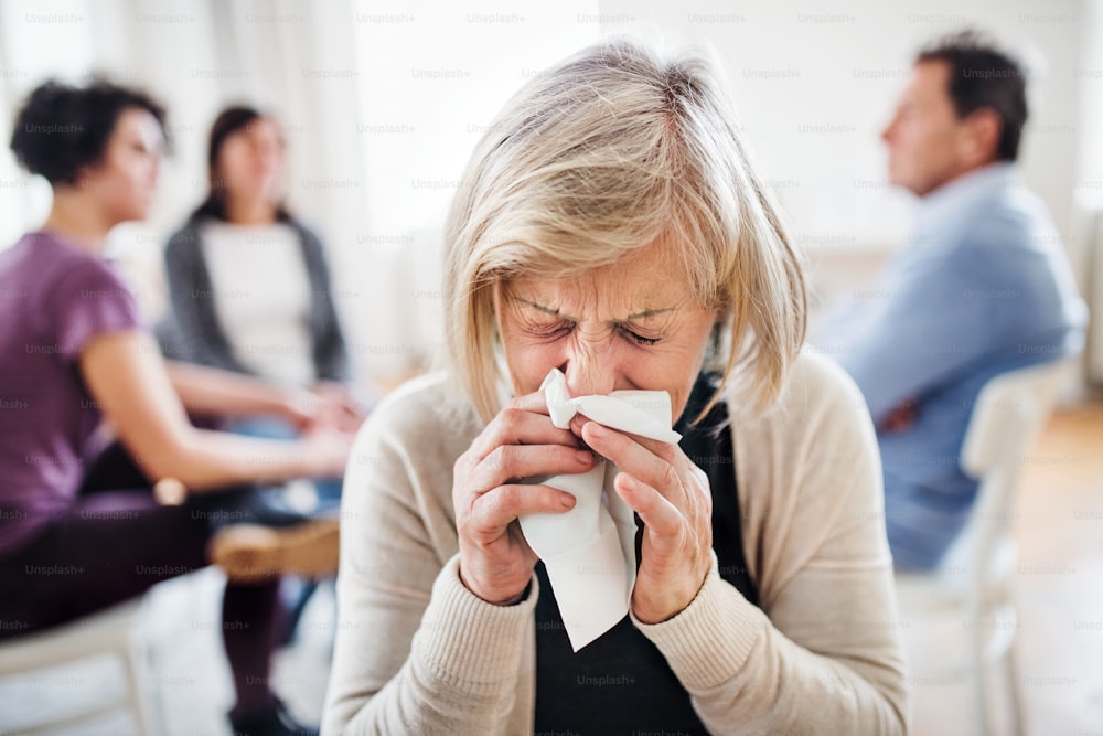 Um retrato de uma mulher deprimida sênior chorando e assoando o nariz durante a terapia de grupo.
