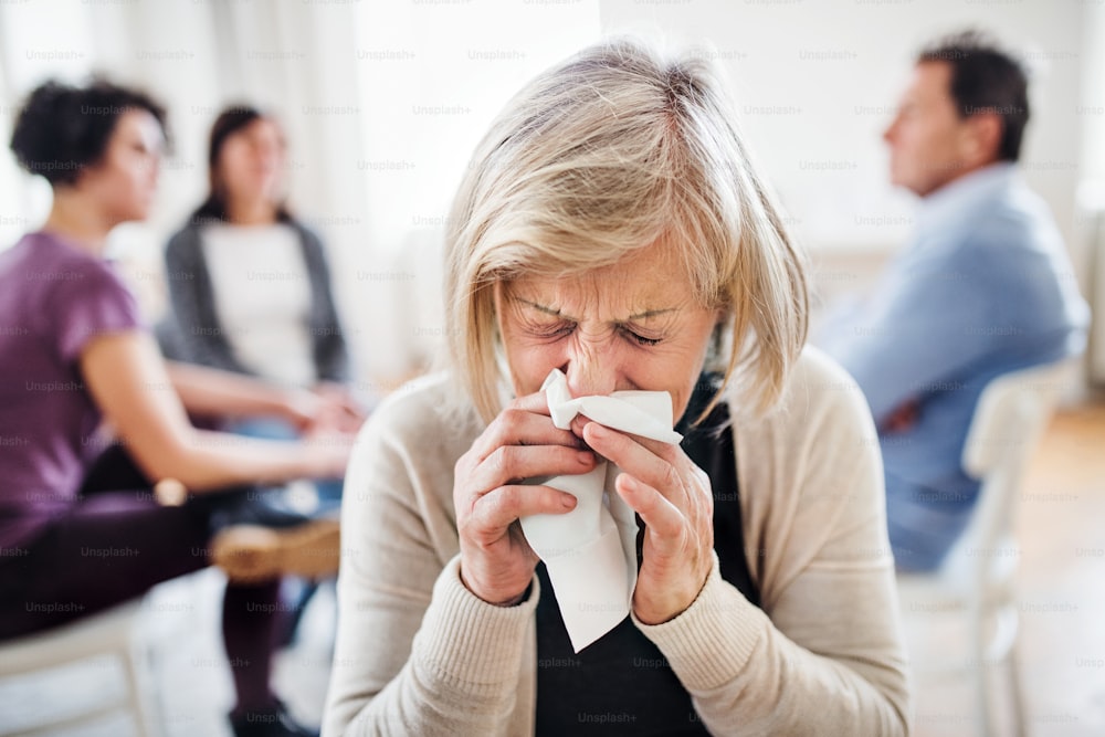A portrait of senior depressed woman crying and blowing nose during group therapy.