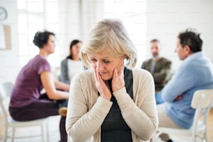 A portrait of senior depressed woman during group therapy, looking down.